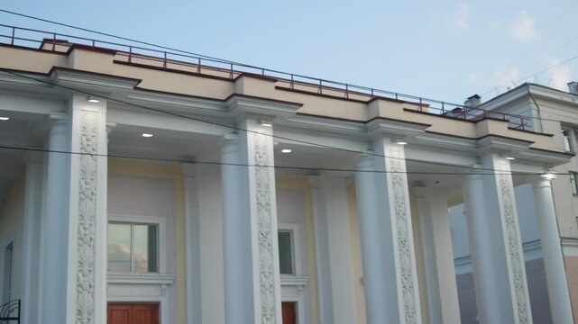 Neoclassical civic building facade with illuminated porch lights and rooftop balustrade at low front angle during dusk
