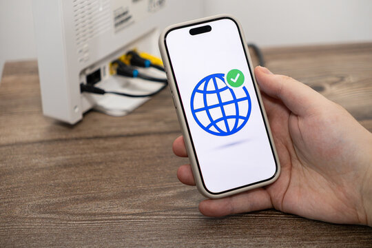A hand holds a smartphone showing a global connection icon with a checkmark near a network router to represent successful internet configuration and reliable wireless home connectivity