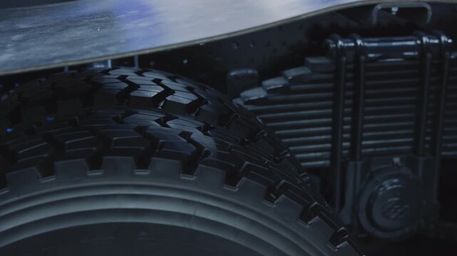 Close-up paired heavy truck tires beneath metal platform showing wheel rim and finned radiator in cool industrial lighting
