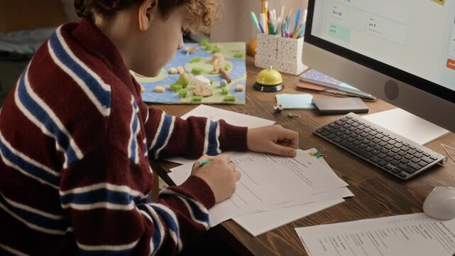 Caucasian teenage boy writing assignment on paper and attending remote tutoring class via desktop computer. Video suitable for online education campaigns and tutoring app ads