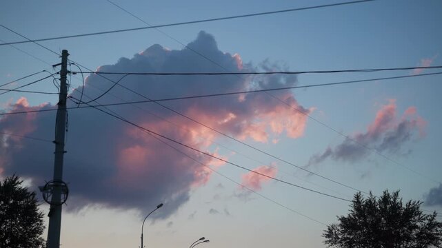 Utility pole and overhead power lines with cumuliform cloud glow at dusk, ground-level upward view