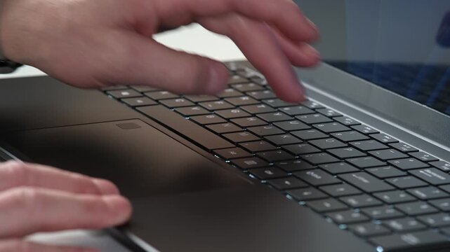 Close-up hands typing on laptop keyboard with fingertip keystrokes in modern office workspace lighting from close angled perspective during daily work routine