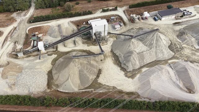 Aerial view of industrial gravel quarry with processing machinery and large piles of sand and gravel in Chivasso, Piedmont, Italy.
