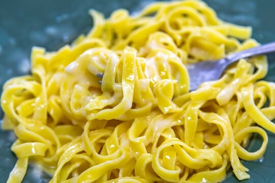 Traditional fettuccine Alfredo &mdash; fresh egg fettuccine pasta coated in a creamy butter and parmesan cheese sauce, served on a green ceramic plate with a fork.