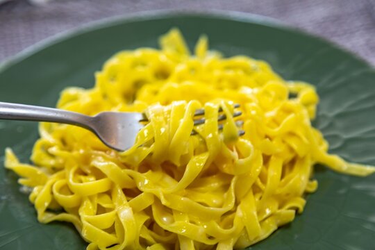 Fettuccine al burro &mdash; fresh egg fettuccine pasta tossed in melted butter and parmesan cheese, served on a dark green ceramic plate, a simple classic of Italian home cooking.