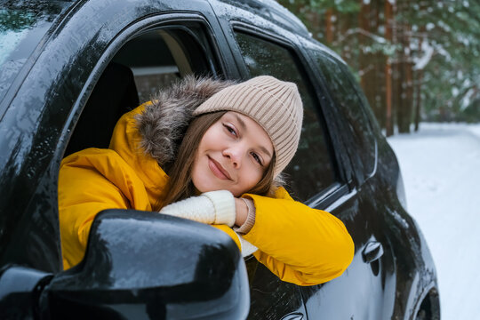Woman driver taking a break beside her car during winter road trip through snowy forest. Temporary rest stop, travel pause and outdoor journey.
