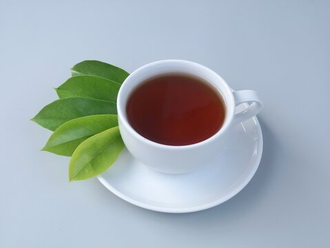 A cup of warm soursop leaf tea served with fresh green soursop leaves on a clean grey background. Healthy herbal drink known for traditional wellness and natural healing benefits