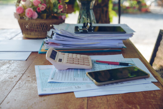 Tax accounting and financial planning with calculator, 1040 form, and smartphone on wooden desk. Report, paperwork, pencil, and binder clip in business workspace.