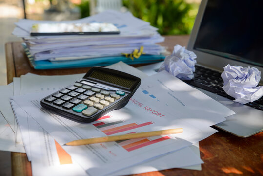 Business calculator and report on wooden desk, with paperwork, laptop, pencil, and paper folder for accounting and financial planning in home office workspace.