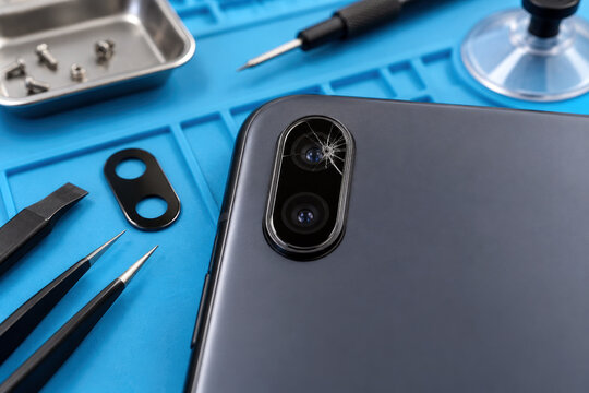 Cracked rear camera lens glass on smartphone with replacement lens cover and tweezers - phone repair camera fix