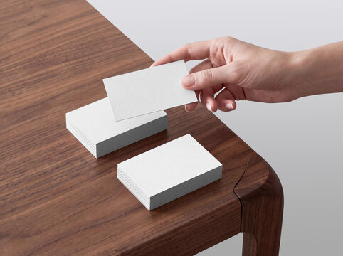 Blank White Business Card Mockup Held above Stacks on Wooden Desk