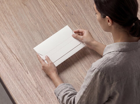 White Envelope Mockup Held by Woman at Wooden Desk for Stationery Design
