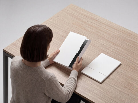 White Document Folder Mockup Held by Woman at Wooden Desk for Branding