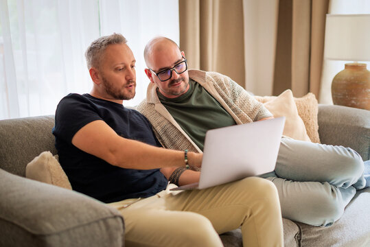 Same-sex male couple with laptop relaxing on a couch at home