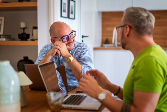 Same-sex male couple working from home, using a laptop together at the table