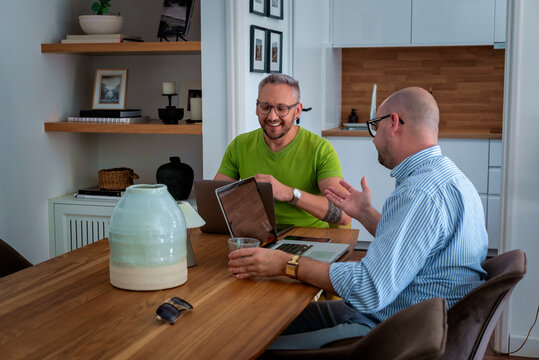 Same-sex male couple working from home, using a laptop together at the table