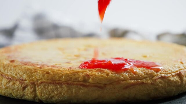 Close up of a traditional Spanish potato tortilla tortilla de patatas with grated tomato being added on top. High quality 4k footage