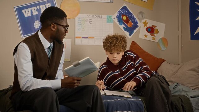 African American male tutor helping Caucasian teenage student with homework assignment. Video suitable for marketing private tutoring platforms and academic learning programs