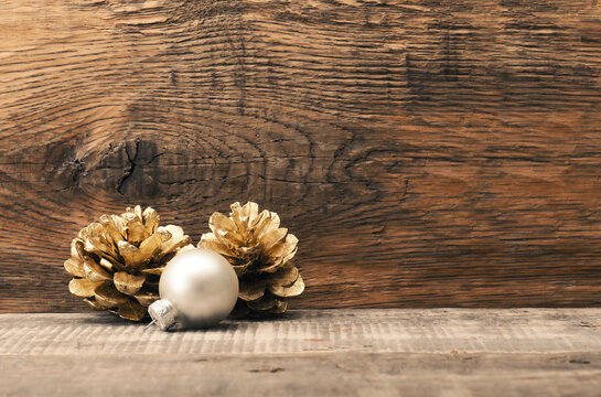 Golden pine cones with a silver Christmas bauble on a wooden background