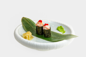 Two gunkan maki sushi with shrimp, spicy sauce and red tobiko on bamboo leaf with wasabi and pickled ginger, white background © Evghenii Blanaru