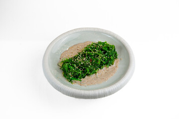 Wakame seaweed salad with sesame and nut sauce on white plate, isolated on white background © Evghenii Blanaru