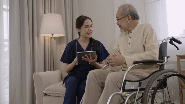 Professional young Asian woman nurse caregiver using a digital tablet to talk and provide advice about healthcare to a senior man patient while sitting in a wheelchair in a special room at hospital. 