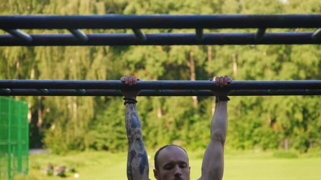 A man jumps from one pull-up bar to another outdoors in a park on a sunny summer day