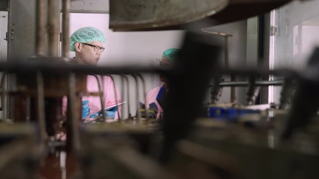 Professional Asian maintenance engineer and technician in food and beverage drink factory in uniform with tablet while talking and discussing machine operation in production line at industry facility.