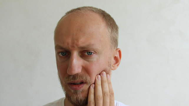 Man touching cheek suffering from severe toothache and sensitive teeth problem