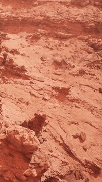 The scene shows a vast expanse of red rock formations under a clear blue sky. The ground is dry and barren, with different layers of rock and texture visible throughout the area.