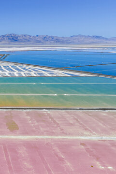 Aerial view of Great Salt Lake solar evaporation ponds with vibrant pink, green, and blue water colors, surrounded by mountains in Ogden, Utah, United States.