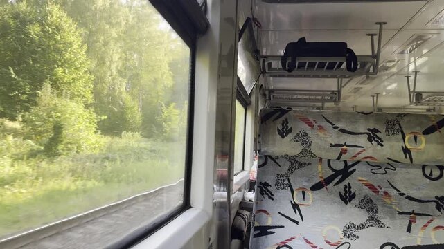 Forest view through a moving passenger train window beside a patterned seat. Rail travel, public transportation and countryside journey background