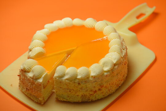 Close-up of a round, layered biscuit cake with creamy filling and fruity mango-apricot jelly. Sweet dessert on an orange background.