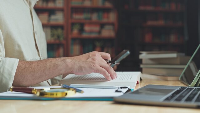 Student conducts academic research across textbook pages, conducting thorough research beside laptop while scholarly research informs study sessions in library.