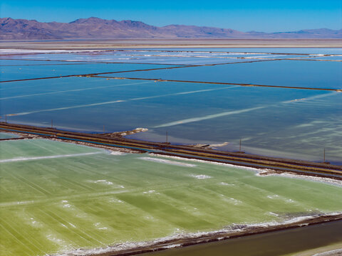 Aerial view of the Great Salt Lake solar evaporation ponds, showcasing vibrant green and blue mineral-rich waters separated by earthen dikes under a clear sky in Ogden, Utah, United States.