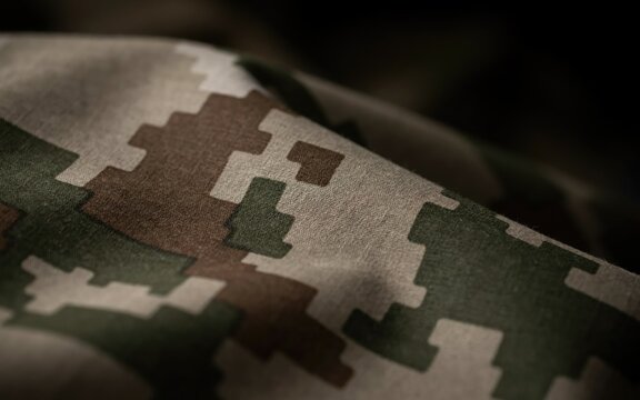 Macro close-up of digital camouflage fabric with pixelated green, brown, and tan patterns