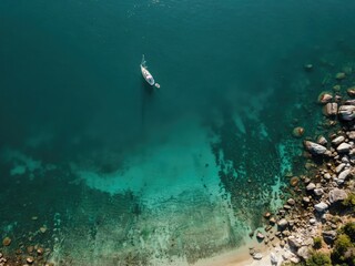 Fototapeta premium Aerial drone view of a white sailboat floating in turquoise tropical water near a rocky coastline