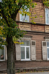 Weathered wooden house facade with tall windows, paneled shutters and horizontal siding, showing exterior joinery and aging timber for residential building maintenance © K