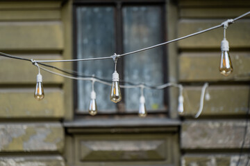 Suspended filament bulbs on festoon cables in front of a building window, showing outdoor decorative electrical fittings used for hospitality venues and event installations © K