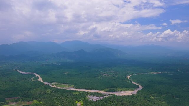 Aerial view of a winding river flowing through lush green tropical landscape with distant mountains under a cloudy sky in Langkat, North Sumatera, Indonesia.