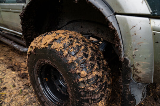 Deep tread blocks on a mud covered SUV tire sit beneath the wheel arch beside exposed suspension parts, showing wheel and chassis components used for rough terrain driving