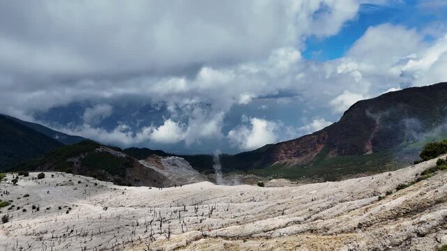 Aerial view of the volcanic landscape of Mount Papandayan with dead trees and lush forest under a cloudy sky in Garut, West Java, Indonesia.