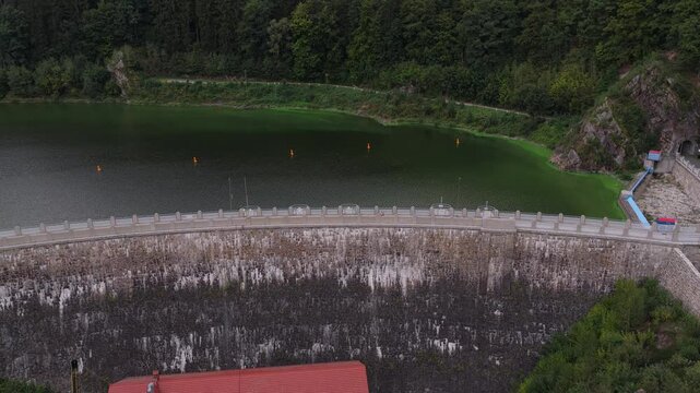 Aerial view of the historic stone Zlotnicka Dam on the Kwisa River, surrounded by lush green forests and calm reservoir waters in Zlotniki Lubanskie, Lower Silesian Voivod, Poland.