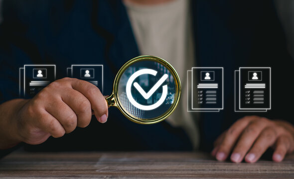Close up hand holding magnifying glass with checkmark icon approving qualified candidate resume profile.