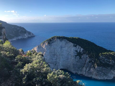 A breathtaking top-down vista of the hidden Navagio bay on Zakynthos, Greece, showcasing towering white cliffs that encircle a secluded sandy beach with a historic shipwreck