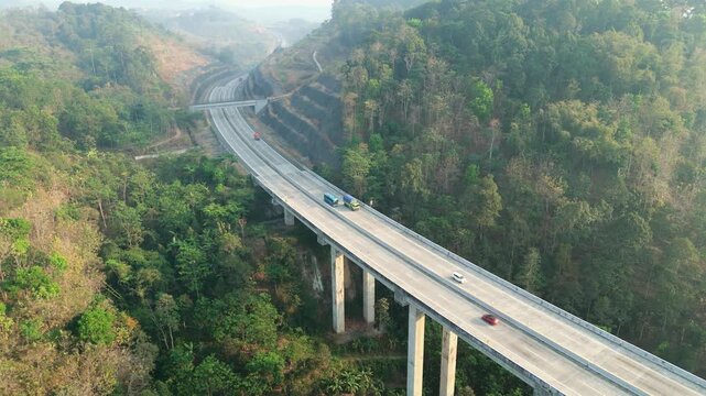 Aerial view of a concrete highway bridge spanning a lush green valley with dense forest and hills in Semarang Regency, Central Java, Indonesia.
