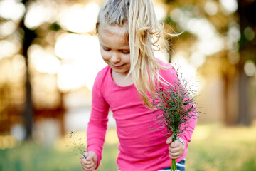 Naklejka premium Park, child and pick grass to explore, play and development in environment on holiday. Smile, girl and kid gather plants in nature for collection, learning or growth on spring vacation with bokeh