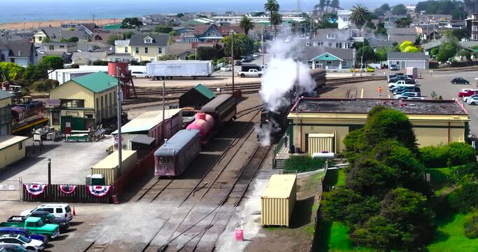 Aerial view of a historic steam train emitting smoke while arriving at the depot in Fort Bragg, California, United States.