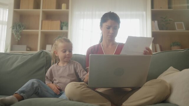 Worried single mother reviewing household bills and bank statements with daughter at home