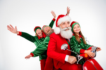 Fototapeta premium Santa Claus and cheerful elves riding a red scooter with a smiling child for a festive Christmas holiday family celebration